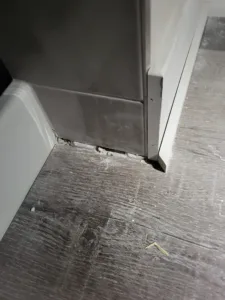 Gray panel beside a white door jamb corner with a small metal bracket, over wood-look flooring.