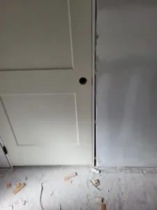 White panel door edge with a lockset bore hole, set against a raw drywall corner.