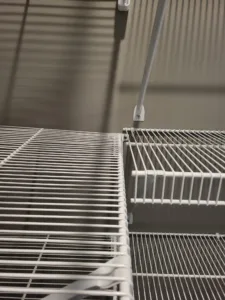 Close-up of white wire shelving with hanging rod at an inside corner connection in a closet.