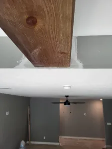 Unfinished raw wood beam end exposed at a wall opening above a ceiling fan
