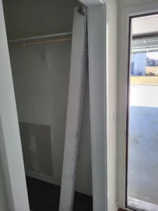 Unfinished closet with door frame legs leaning inside, bare drywall walls, exterior visible outside.