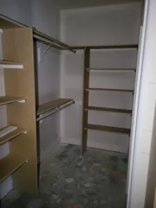 Walk-in closet with tiered angled shelves and rod brackets installed, unfinished particleboard.