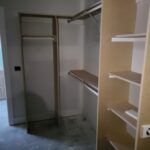 Walk-in closet with multiple shelves, hanging rods, and support structure installed; raw wood and drywall ready for paint.
