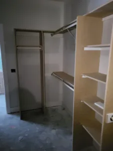 Closet shelving with natural wood tone shelves and hanging rods installed, unfinished, concrete floor.