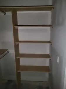 Raw wood closet shelf unit with five particle board shelves and a support post, unfinished.