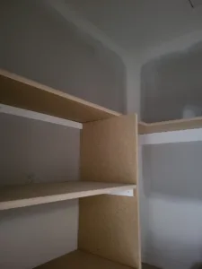 Particle board closet shelf with a bullnose edge and raw wood trim, unpainted, at an inside corner.