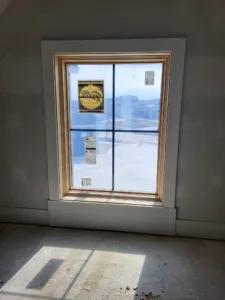 Wood casing installed around a four pane window, light toned and trimmed neatly at the sill.