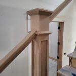 Finished wood newel post with decorative cap at stair landing, raw wood ready for stain or paint.