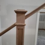 Finished wood newel post with cap and base trim supporting stair handrail.