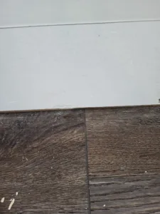 LVP flooring installed, meeting white baseboard trim at the wall base
