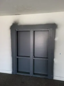 Dark framed glass double doors set in an opening, with black paint overspray on the wall