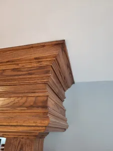 Stained oak decorative header with stacked built-up molding profiles atop a paneled post, finished.