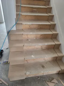 Interior stair with particleboard covered treads and oak end caps being fitted to the open left side