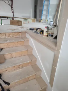Unfinished wood stepped cap trim installed atop a stair knee wall, ready for finishing