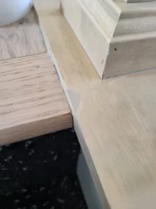 Raw wood trim resting on a dark stone surface, showing an unfinished molded edge profile