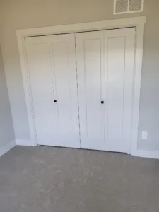 Painted white double bifold closet door closed, black square knobs, white casing and baseboard
