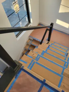 Overhead view of a black metal newel post and handrail above taped wood treads
