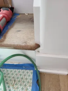 Primed white baseboard installed at a wall-to-floor junction, protective tape on the floor nearby
