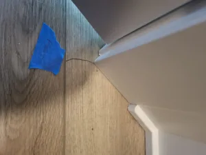 Wood tone baseboard with a curved profile mitered at an outside corner over matching flooring