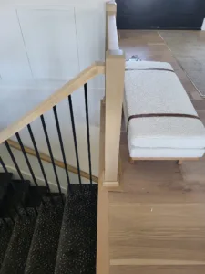 Stair railing with a wood cap rail, vertical iron balusters, and a built in bench nearby