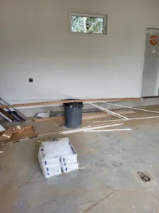 Job site room in progress with baseboard trim materials staged near a small window