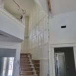 Staircase mid-construction with finished skirt boards, raw treads/risers, and protective coverings in place.