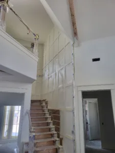 Paneled wall with plastic sheeting taped for protection, staircase visible below.