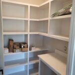 Custom built-in shelving unit with painted white face frame, multiple shelves, and integrated countertop work surface in closet.