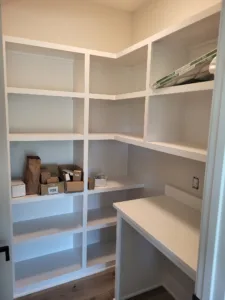 Corner closet shelving with cubbies over a built in desk, painted white, storage boxes on shelves