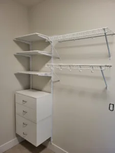 Wire closet shelving with hanging rods above a white four-drawer storage tower, painted walls.