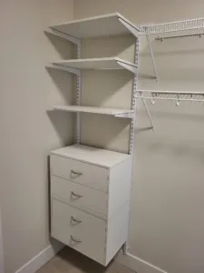 Metal track shelving with three brackets and a hanging rod above a white painted four drawer unit