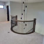 Completed curved iron baluster railing with dark wood handrail and newel posts installed on staircase.