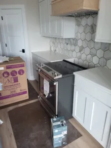 Kitchen mid-install with painted cabinetry, hexagon tile backsplash, and appliances staged