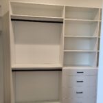 Painted face-frame closet shelving with hanging rods, open shelves, and drawer stack with black hardware.