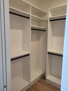 Finished walk-in closet with painted white shelving, adjustable shelves, and black hanging rods