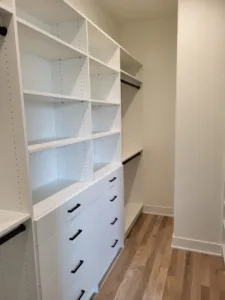 Built-in closet shelving with a painted white finish and lower drawers with black pulls