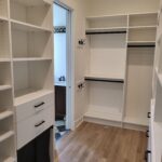 Completed walk-in closet with white face-frame shelving, hanging rods, and black hardware installed.