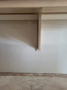 Wood support bracket beneath an unfinished shelf in a closet, ready for paint