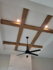 Dark stained wood beams crossing in an X pattern above a fan and stone fireplace column