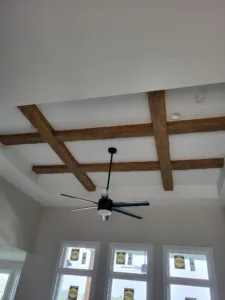 Dark stained ceiling beams in a grid above a ceiling fan and a row of windows