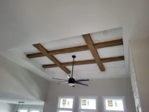 Dark stained ceiling beams crossing in a grid within a tray ceiling above windows