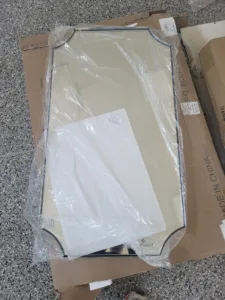 Rectangular framed mirror still wrapped in plastic, resting on its shipping box before installation