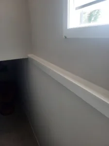 Painted white horizontal trim rail below a window, with dark accent wall paint underneath.