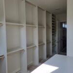 Face-frame closet shelving with multiple tiers and hanging rods, primed white, ready for paint.