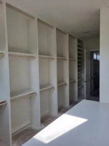 Primed white built in shelving with multiple tiers along a wall, ready for paint