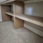 Custom built-in shelving with multiple tiers, vertical dividers, and particle board shelves ready for finish.