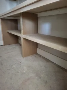 Unfinished particleboard closet shelves with center divider under an angled ceiling, raw wood.