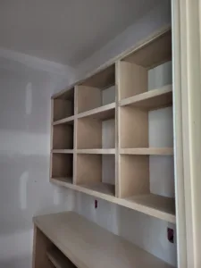 Wall-mounted cubby grid with square openings above a lower shelf, unfinished wood, molding visible.