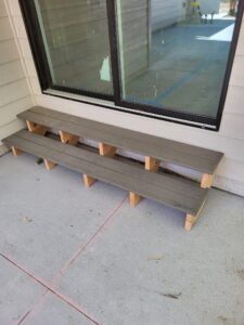 Two low open riser patio steps with gray composite treads on wood block supports in front of a sliding glass door