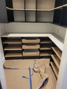 Walk-in closet cabinet build in progress, black boxes, open shelving, and wood drawer fronts